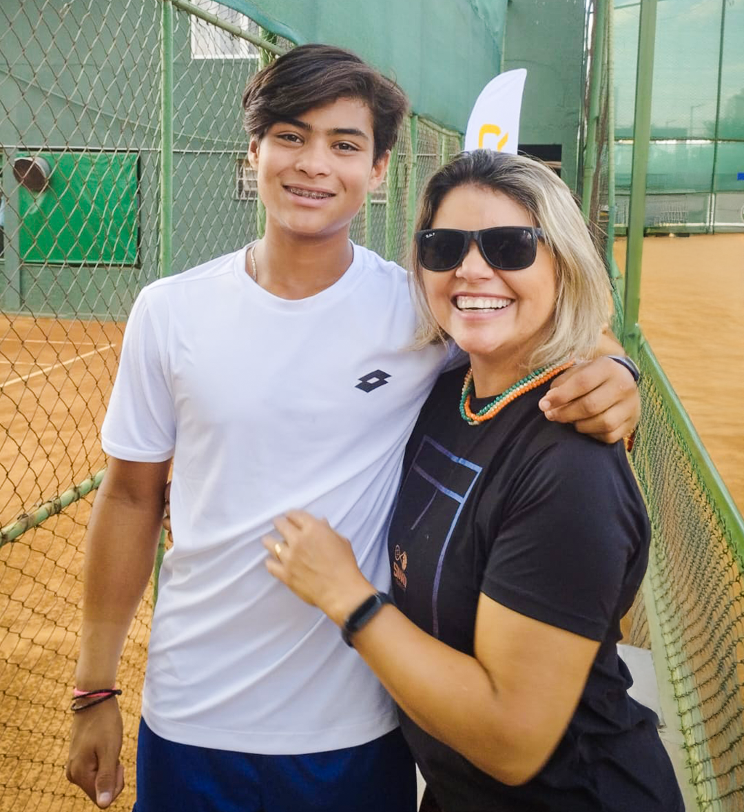 Aluna e jovem atleta posando juntos na área lateral das quadras da Smash.