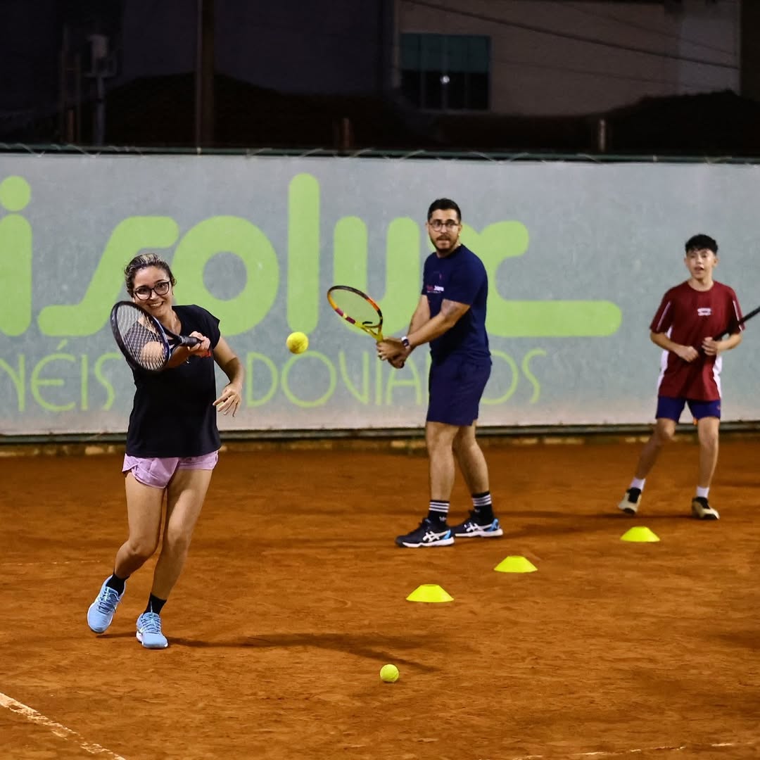 Professor orientando alunos em quadra de saibro.
